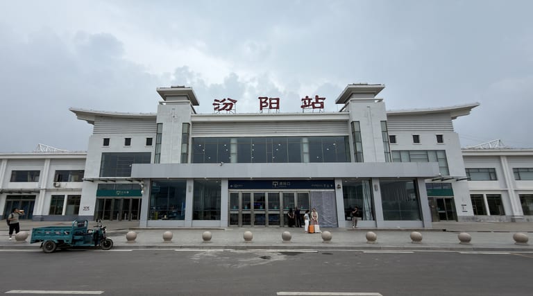 汾阳站正面的白色玻璃幕墙建筑，红色'汾阳站'立体字，几名旅客拖着行李准备进站