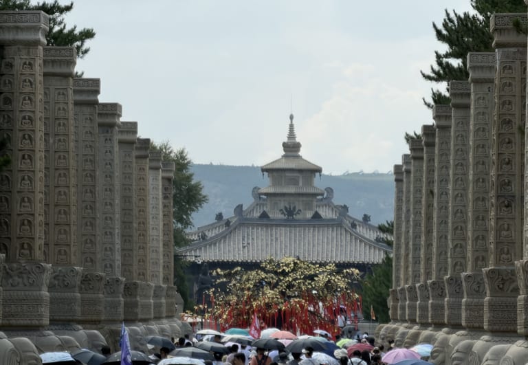 昙曜广场入口的柱廊,两列刻满小佛龛的石柱夹道延伸,远处可见一座楼阁,前景是举伞的游客