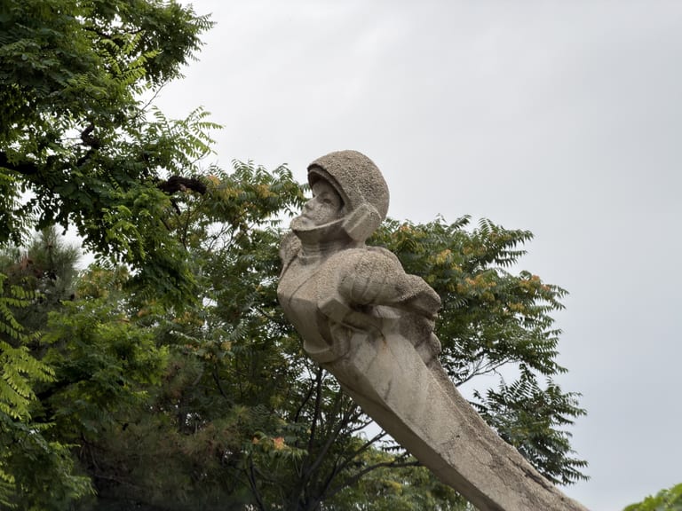 大同儿童公园里的贾樟柯电影宇航员雕像,灰色石雕,前倾姿态仰望天空,双臂在胸前交叉抱持长形物件