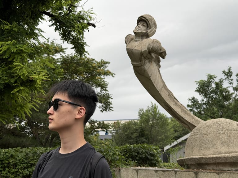 大同儿童公园宇航员雕像下的合影,合影者侧身望向画面左侧,背景是深色花岗岩骑马人物雕像